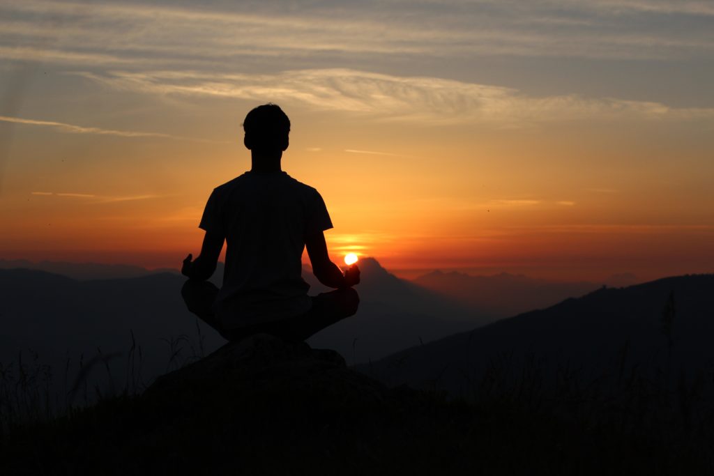 A guy meditating on the mountain peak during the sunset
